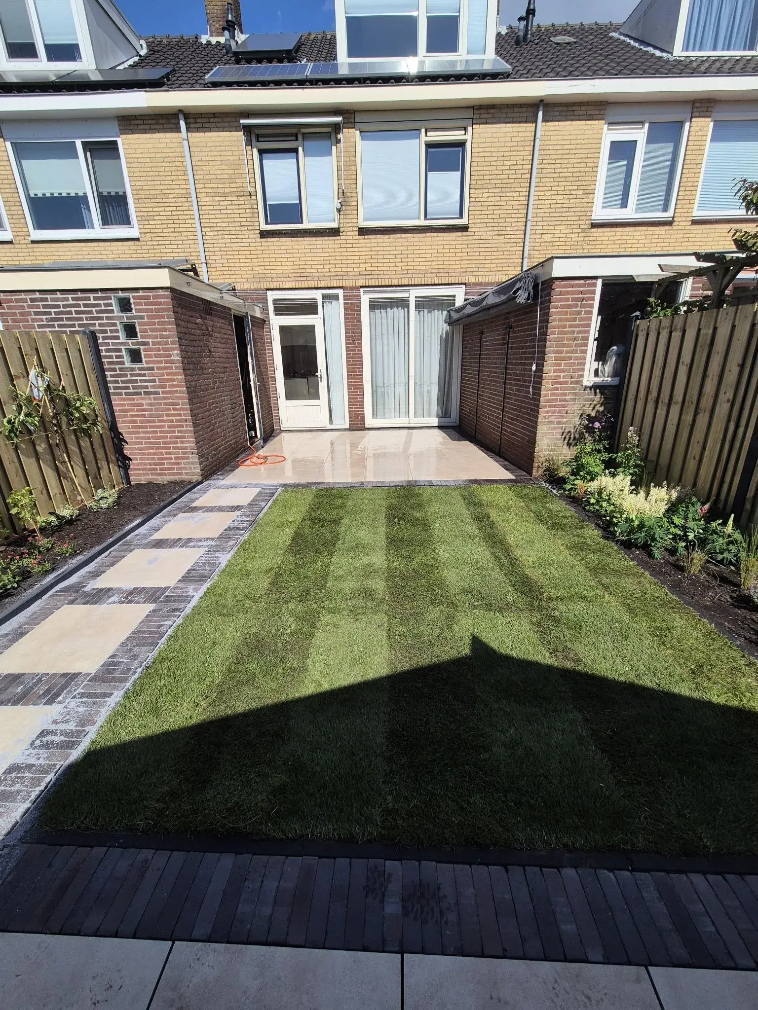 Achtertuin met gazon, tegelpad, terras en beplante randen