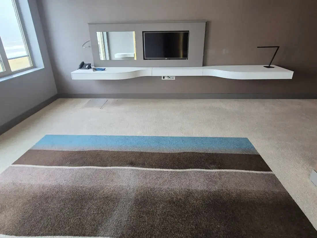 Kamer met vloerbedekking, een zwevend wit wandmeubel en een televisie aan een grijsbruine wand