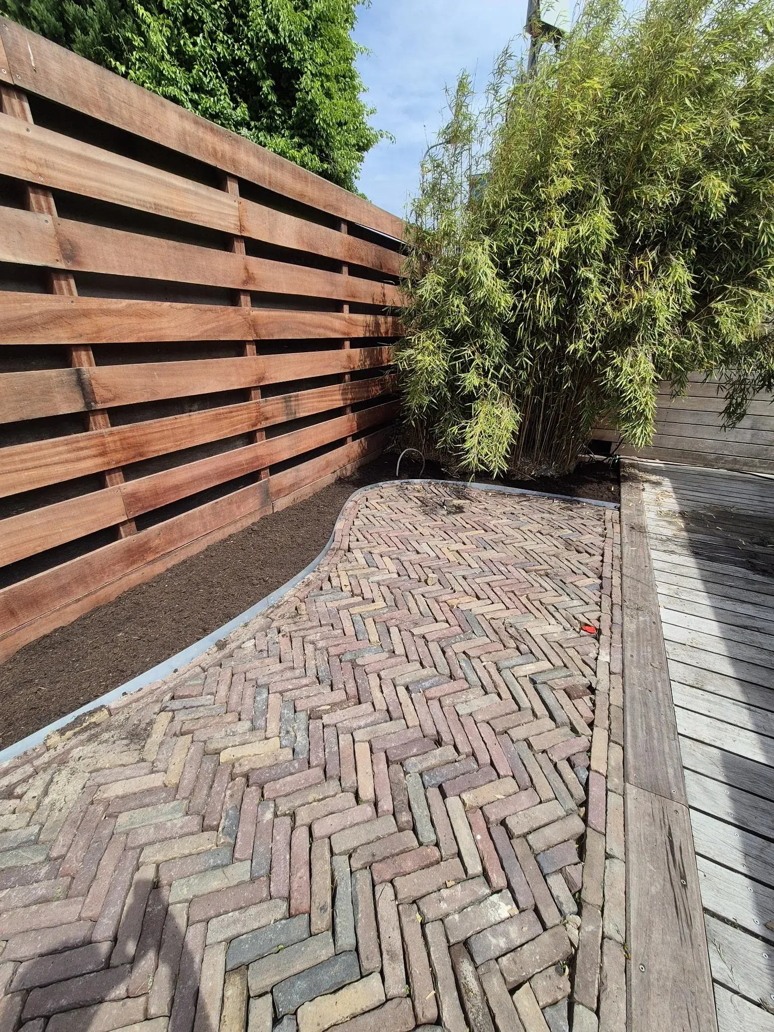 Visgraatbestrating langs een houten schutting en bamboe