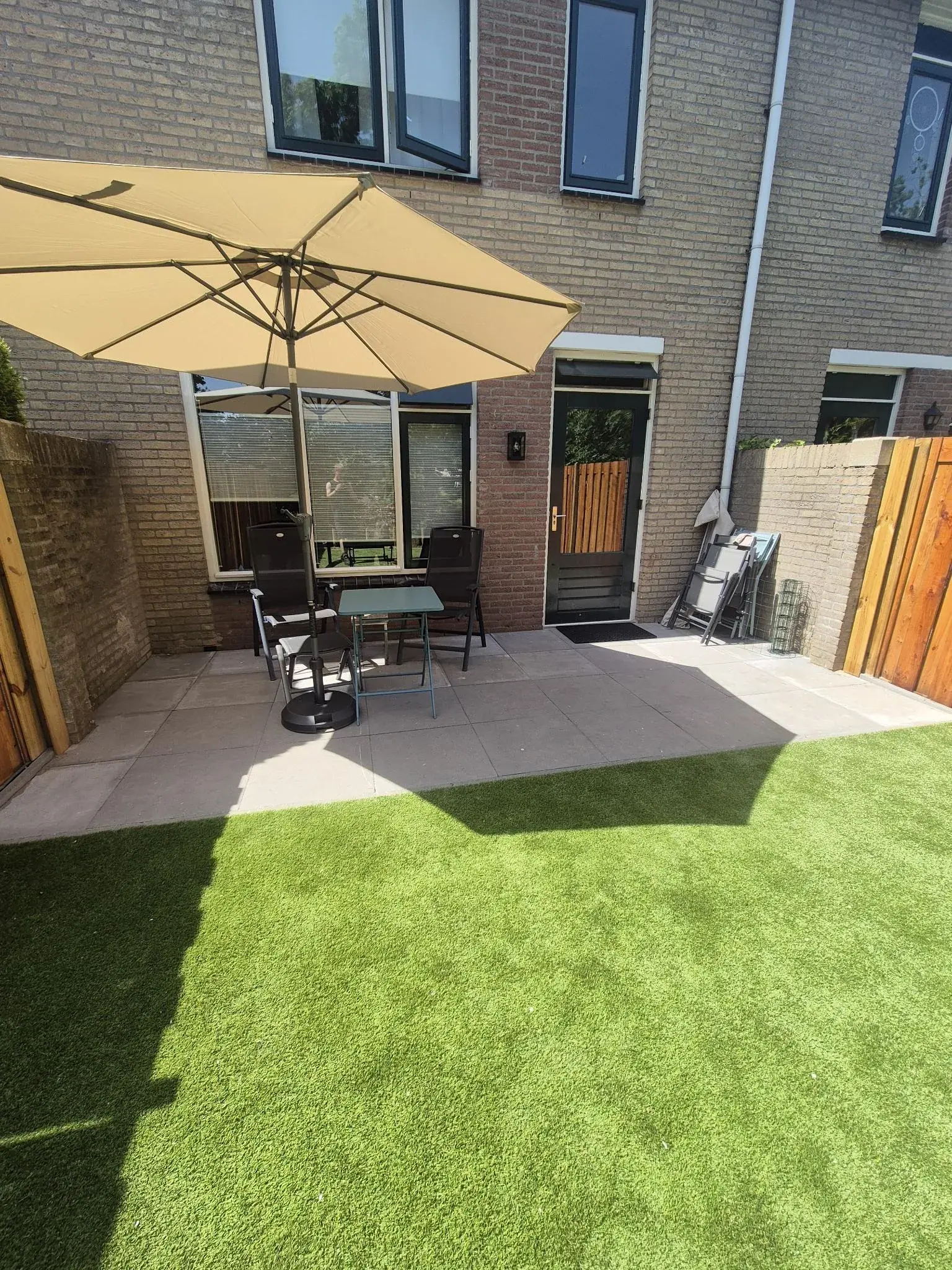 Terras met parasol, lichte tegels en kunstgras