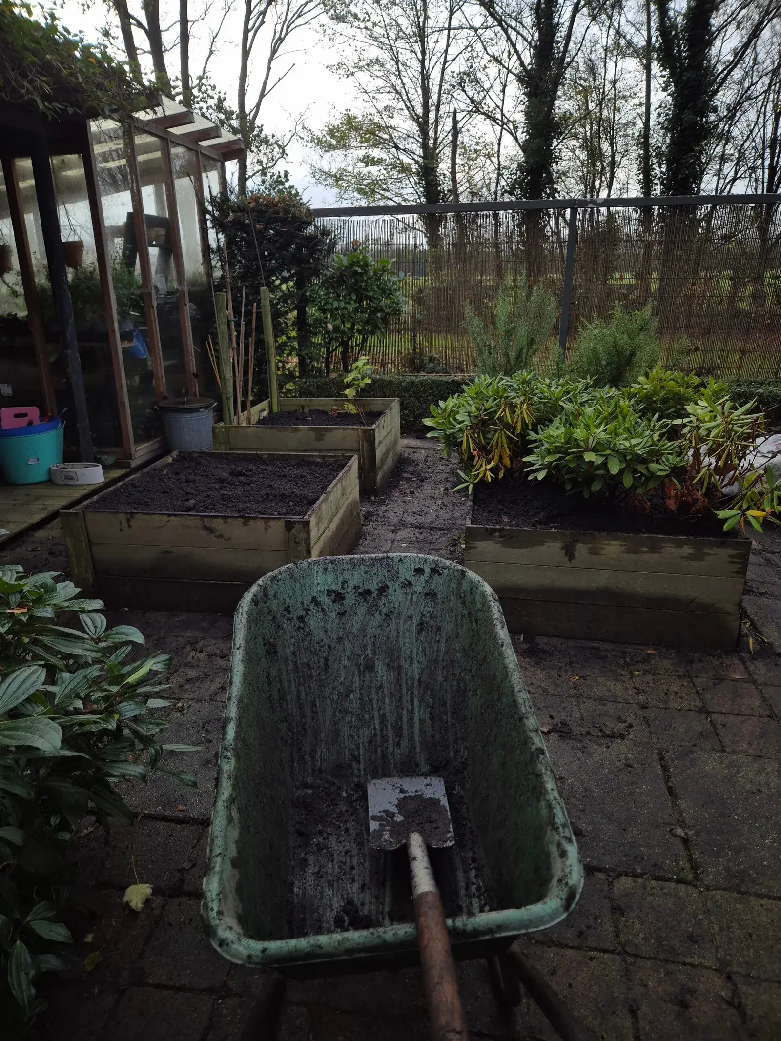 Kruiwagen met een schep bij houten plantenbakken tijdens tuinwerkzaamheden